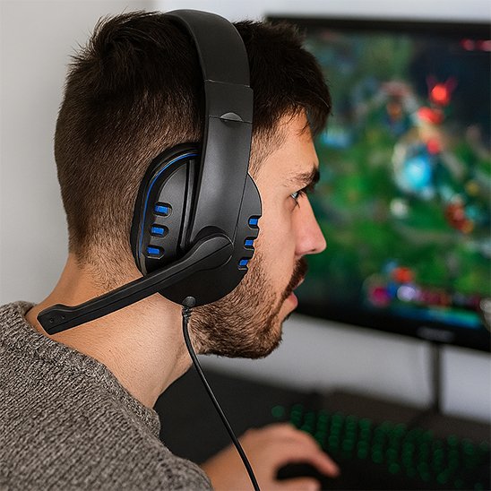 Casque gaming noir avec accents bleus, microphone flexible, porté par un homme face à un écran d'ordinateur flou.