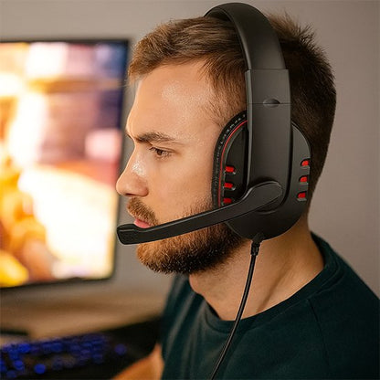 Casque gaming noir avec micro flexible et accents rouges porté par un homme, arrière-plan flou d'écran d’ordinateur.