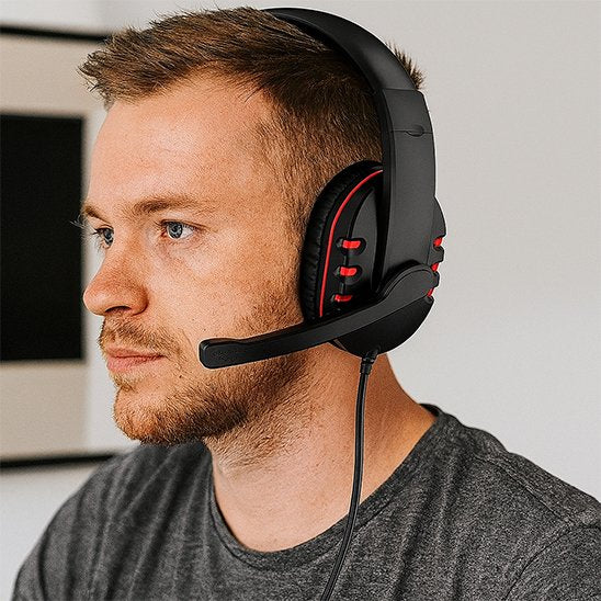 Casque gaming noir avec micro ajustable et détails rouges porté par un homme aux cheveux courts, t-shirt gris.