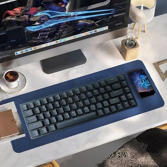 Clavier ergonomique noir compact sur tapis bleu, smartphone posé sur le côté droit, clavier devant écran d’ordinateur blanc.