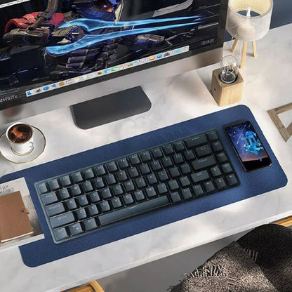 Clavier ergonomique noir compact sur tapis bleu, smartphone posé sur le côté droit, clavier devant écran d’ordinateur blanc.