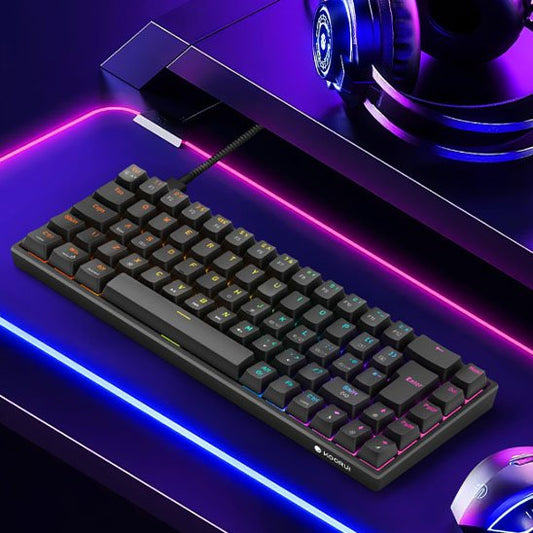 Clavier mécanique compact noir avec éclairage RGB sous les touches, posé sur un bureau lumineux avec des bandes LED rose et.