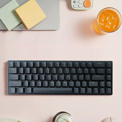 Clavier compact mécanique noir avec touches rétroéclairées, posé sur bureau rose avec bloc-notes, calculatrice et verre de.