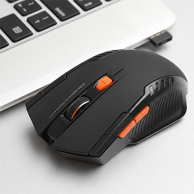 Souris gamer sans fil noire avec molette et boutons orange, posée à côté d’un clavier d’ordinateur portable gris et recevant .