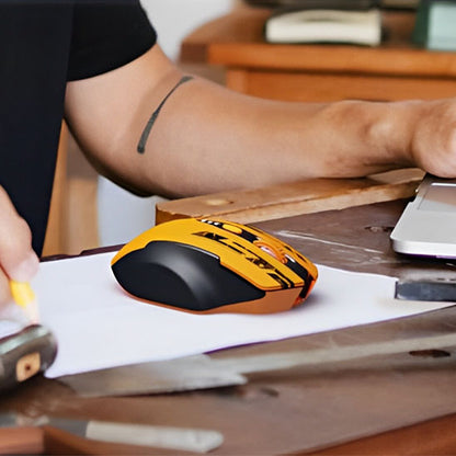Souris sans fil ergonomique noire et orange posée sur un bureau en bois à côté d’un bras et d’un ordinateur portable gris.