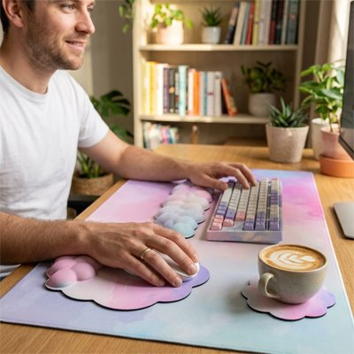 Tapis de souris gris clair avec repose-poignet gel rose en forme nuage, tasse de café latte sur sous-verre assorti, clavier.